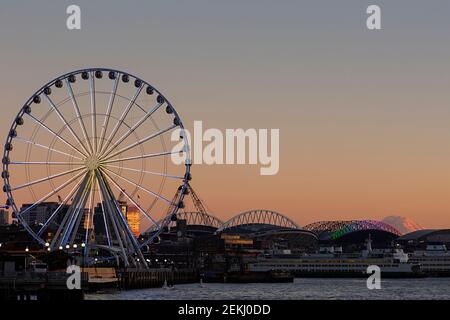 WA19346-00...WASHINGTON - le front de mer de Seattle au coucher du soleil, y compris la Grande roue, Colman Ferry Dock, Lumen Field, T-Mobil Stadium et Mount Rainie Banque D'Images