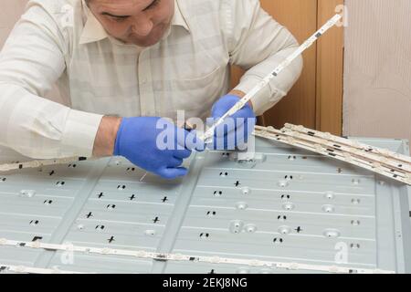 Réparation du téléviseur LCD dans le centre de service. Master retire les barrettes de LED avec les lampes du boîtier du moniteur. Banque D'Images