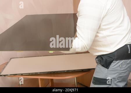 Démontage du téléviseur LCD pour diagnostic et réparation. L'ingénieur retire soigneusement la vitre de la matrice du grand moniteur. Banque D'Images