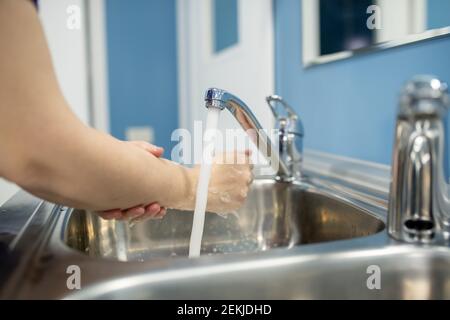 Jeune femme assistante, infirmière ou chirurgien se lavant les mains sur l'un des deux éviers métalliques avant ou après l'intervention médicale à l'hôpital Banque D'Images