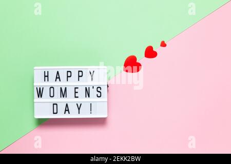 Tableau lumineux avec inscription Happy Women's Day, trois coeurs rouges de différentes tailles sur fond pastel rose et vert, espace copie. Horizontale. Internat Banque D'Images