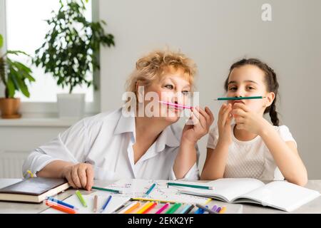 Petit-enfant heureux avec grand-mère ayant l'amusement, dessin de crayons de couleur, assis ensemble à la maison, riant la petite fille d'âge préscolaire avec sourire peinture de grand-mère Banque D'Images