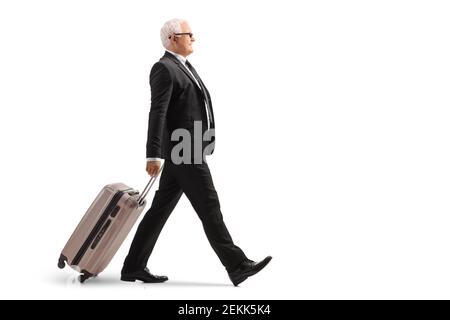 Photo pleine longueur d'un homme d'affaires mûr marchant et tirer une valise isolée sur fond blanc Banque D'Images