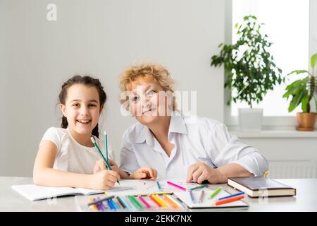 Petit-enfant heureux avec grand-mère ayant l'amusement, dessin de crayons de couleur, assis ensemble à la maison, riant la petite fille d'âge préscolaire avec sourire peinture de grand-mère Banque D'Images