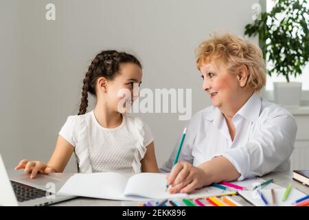 Petit-enfant heureux avec grand-mère ayant l'amusement, dessin de crayons de couleur, assis ensemble à la maison, riant la petite fille d'âge préscolaire avec sourire peinture de grand-mère Banque D'Images