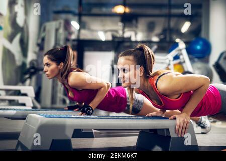 Deux jeunes motivés athlétiques attirantes sportives focalisées filles actives faisant des push-up sur les steppers dans la salle de gym moderne. Banque D'Images