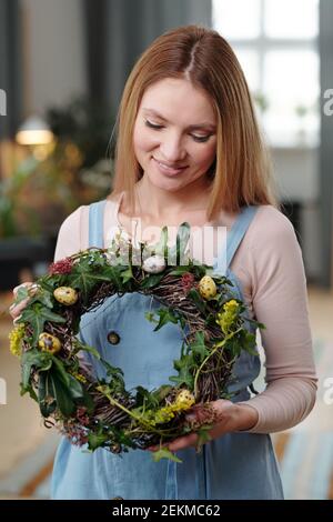 Bonne jeune femme regardant la couronne dans ses mains faites De fleurs et d'oeufs pour les vacances de Pâques Banque D'Images