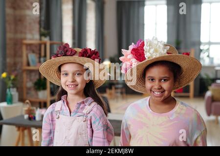 Portrait de deux petites filles dans de beaux chapeaux avec des fleurs sourire à l'appareil photo Banque D'Images