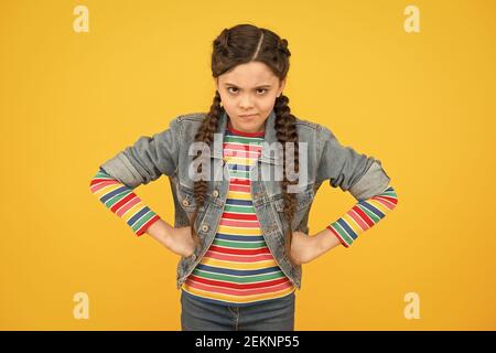 Dans la mauvaise humeur. Moody petit enfant fond jaune. Coiffure tressée pour bébé. Petite fille dans un style décontracté. Petit enfant avec les mains sur les hanches. Mode tendance. Tendances élégantes. Salon de coiffure. Banque D'Images