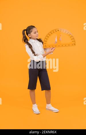 Carré avec réglage d'angles. Petite fille à l'aide de triangle pour mesurer les angles en degrés sur fond jaune. Petit enfant scolaire rapporteur pour la géométrie leçon. L'apprentissage de l'utilisation d'angles. Banque D'Images