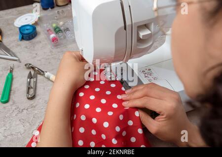 portrait des mains sur une femme latine attrayante utilisant une machine à coudre, plus des ciseaux, des fils, du tissu, faisant des vêtements à la maison comme petite femme d'affaires Banque D'Images