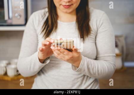 Gros plan sur la section médiane de la femme caucasienne inconnue utilisant le mobile téléphone à la maison - mains de femmes tenant un smartphone pour taper un message ou en naviguant sur internet Banque D'Images