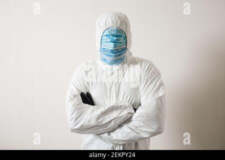 un homme dans un costume de protection accroché à des masques médicaux posant sur un fond de mur montrant divers gestes avec son doigts Banque D'Images