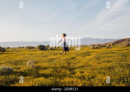 Joyeuse jeune femme dansant dans le champ de fleurs du désert Banque D'Images