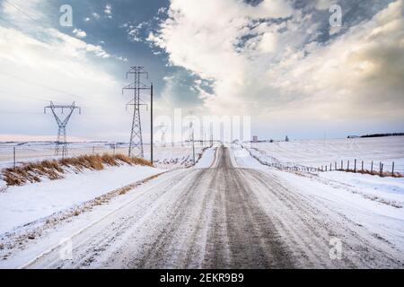 Une route de gravier rurale le long des lignes électriques et de la transmission électrique Tours dans le comté de Rocky View Alberta Canada pendant l'hiver Banque D'Images