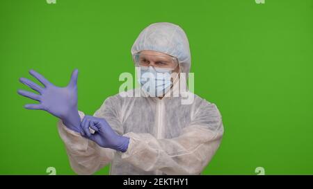 Un professionnel de la santé se tenant isolé sur fond de chroma clé et met des gants de main. Jeune médecin en uniforme de combinaison de protection PPE. Coronavirus, pandémie de quarantaine covid-19. Portrait médical Banque D'Images