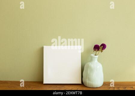 Toile blanche et vase de fleurs sèches sur table en bois. Fond vert kaki. Espace de copie Banque D'Images