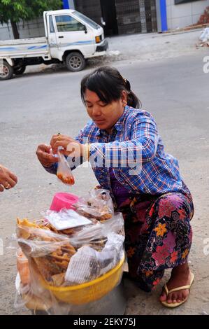 La femme birmane vend des produits de la nourriture pour le peuple birman et les voyageurs étrangers qui marchent choisissent et achètent dans le bazar du marché local À côté de la route à Mandalay D. Banque D'Images