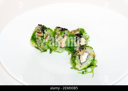 Cuisine japonaise, petits pains à sushis européens au fromage à la crème, saumon et chuka. Les petits pains à sushis verts, accompagnés de la cuisine chuka et de la sauce au sésame, sont servis sur une assiette blanche Banque D'Images