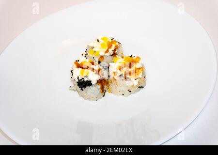 Les sushis roulés california avec du fromage à la crème sont sur une assiette blanche. Cuisine japonaise, petits pains à sushis européens avec fromage à la crème, saumon et avocat Banque D'Images