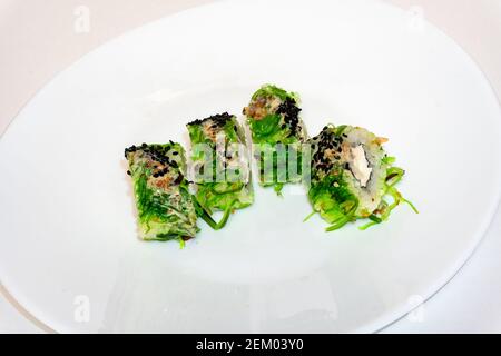 Les petits pains à sushis verts, accompagnés de la cuisine chuka et de la sauce au sésame, sont servis sur une assiette blanche. Cuisine japonaise, petits pains à sushis européens au fromage à la crème, saumon et chuka Banque D'Images