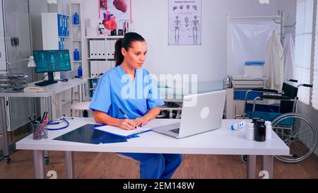 L'infirmière se fait le récevant des résultats de santé des patients, prenant des notes sur le presse-papiers, lisant sur un ordinateur portable à l'hôpital. Médecin en médecine uniforme rédaction de la liste des patients consultés, diagnostiqués, faisant de la recherche. Banque D'Images