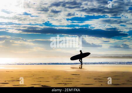 Silhouette de surfeur marchant le long de la plage avec surf Banque D'Images