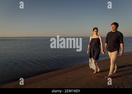 Jeune couple d'amoureux marchant le long de la plage du soir. Copier l'espace. Banque D'Images