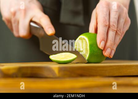 Femme coupant de la chaux dans la cuisine, de l'eau de citron, de l'eau rafraîchissante avec de la chaux et du citron, concept de saine alimentation Banque D'Images