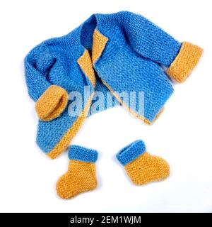 Pull bleu et jaune tricoté à la main avec chaussons assortis pour bébés affichés sur un fond Uni Banque D'Images