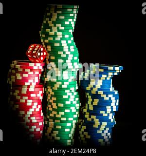 Piles de jetons de poker colorés avec un dé rouge sur un fond sombre, parfait pour les amateurs de jeux et les thèmes de casino Banque D'Images