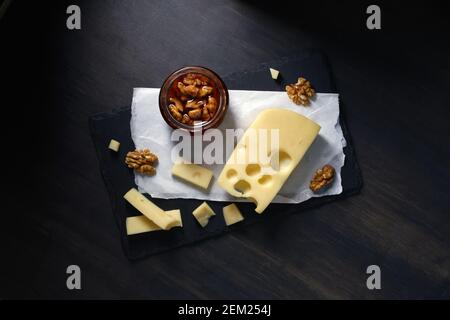 le fromage semi-dur maasdam coupé en tranches se trouve sur la plaque de pierre avec miel et noix sur fond sombre Banque D'Images