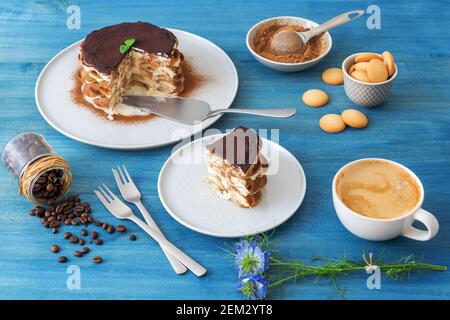 Tiramisu maison ronde, sans cuisson dessert sucré traditionnel italien. Tableau bleu avec du gâteau, bol avec la poudre de cacao, biscuits éponge ronde, les grains de café Banque D'Images