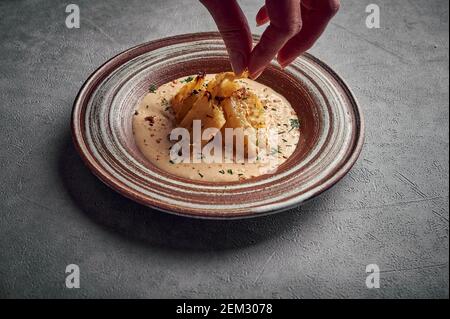 La main de la femme saupoudrer avec de l'aneth cuit au chou-fleur maison dans la sauce au fromage gruyère et de l'huile d'olive dans une plaque en céramique sur un fond sombre, nourriture saine, espace de copie Banque D'Images