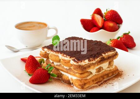 Tiramisu, sucré italien maison, dessert sans cuisson, coupe de gâteau sur une petite assiette ornée de menthe fraîche et quelques vraies fraises, une tasse de café et Banque D'Images