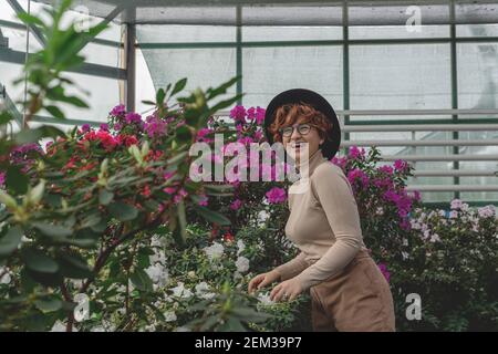 Une belle fille de taille plus dans un chapeau rie parmi les plantes vertes de serre Banque D'Images