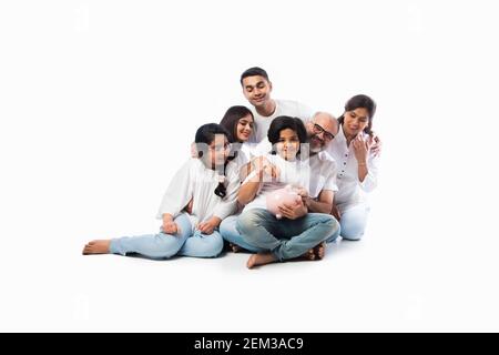 Famille indienne multigénérationnelle de six personnes tenant une tirelire tout en portant des chiffons blancs et se tenant contre un mur blanc Banque D'Images