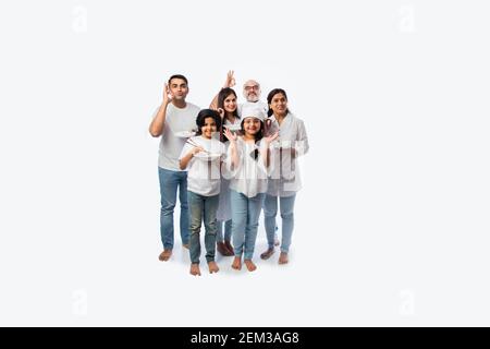 Famille indienne multigénérationnelle de six personnes tenant une assiette vide et des bols tandis que la petite fille chef porte le chapeau Banque D'Images