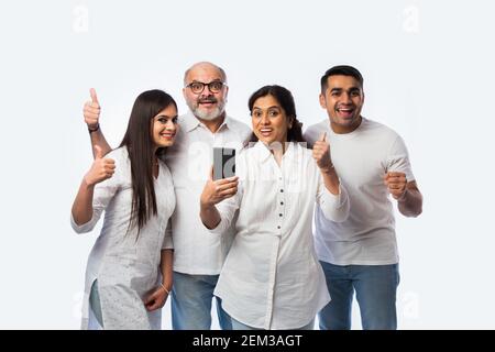 Jeune couple indien avec des parents utilisant ou tenant un smartphone avec des expressions heureuses, debout contre le blanc Banque D'Images