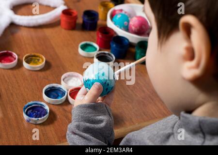 Un petit garçon peint des œufs de gouache. Se préparer pour Pâques, joyeux enfant peint avec les couleurs d'un œuf de poulet. Banque D'Images