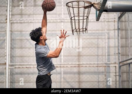 jeune homme asiatique adulte joueur de basket-ball essayant une dunk sur un terrain extérieur Banque D'Images