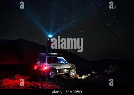 Une femme avec sa lumière de tête regarde à ciel étoilé dans la voiture tout-terrain dans le désert Banque D'Images