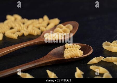 Cuillères en bois pleines de pâtes de girandole et de tonde farfalle crues Banque D'Images
