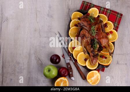 Canard entier cuit avec romarin frais et oranges sur plaque d'argile, fond de bois gris, canard rôti, espace de copie Banque D'Images