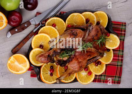 Canard entier cuit avec romarin frais et oranges sur plaque d'argile, fond de bois gris, canard rôti, espace de copie Banque D'Images