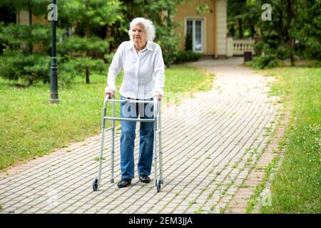 Femme senior utilisant l'équipement de marche pour l'aider avec un promenade dans le parc Banque D'Images