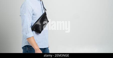 Homme dans une chemise bleue avec un sac en cuir noir fait main sur son épaule. Sac banane de créateur sombre. Homme dans un studio. Petit sac confortable pour la marche. Banque D'Images