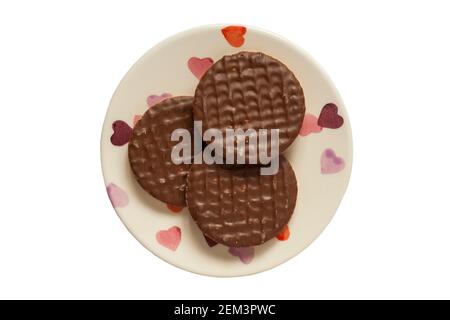 Trois biscuits digestifs au chocolat au lait McVitie's sur l'assiette avec des coeurs sur fond blanc Banque D'Images