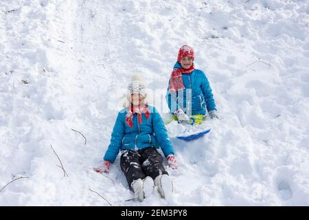 Deux filles ont roulé sur la colline et s'asseyant dans le neige regarder joyeusement dans le cadre Banque D'Images