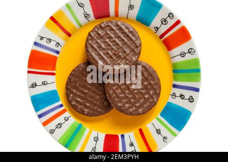 Trois biscuits McVitie's Milk chocolat digestitifs sur un ensemble d'assiettes colorées sur fond blanc Banque D'Images